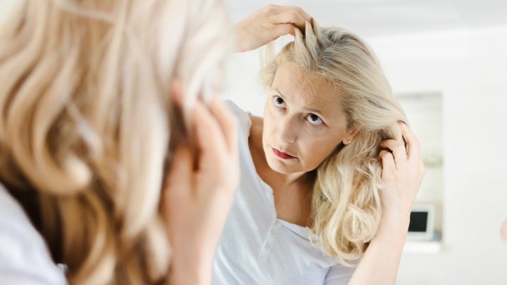 woman with blonde hair checking her roots in mirror