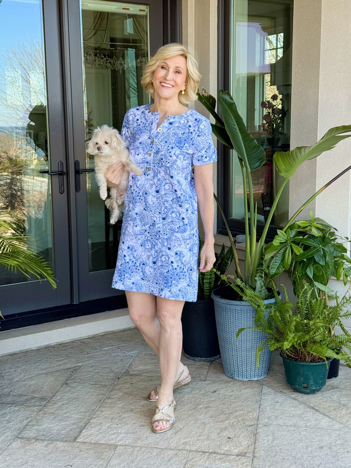 Deborah Boland in a classic straight fit shift dress featuring a royal blue and white animal motif with gold hardware at the neckline and gold sandals.