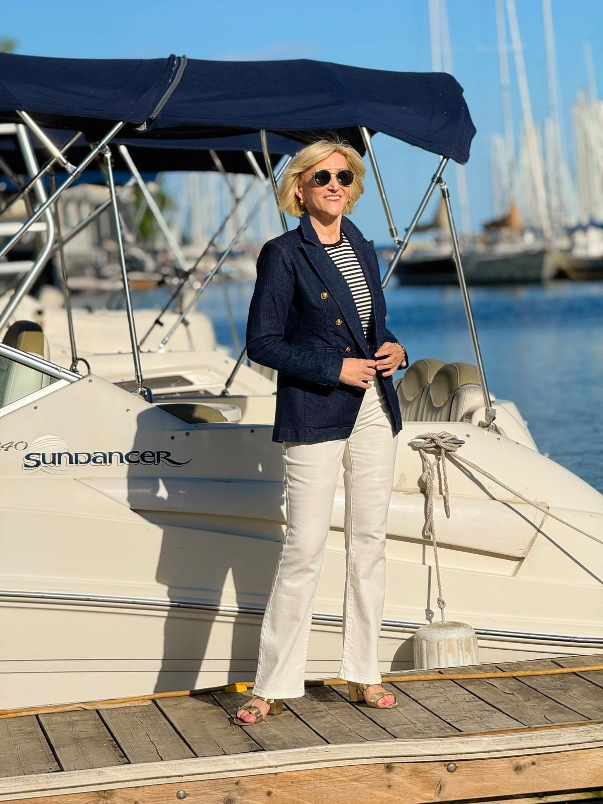 Deborah Boland wearing a navy blazer, striped tee, white jeans, and neutral sandals in a timeless nautical style outfit.