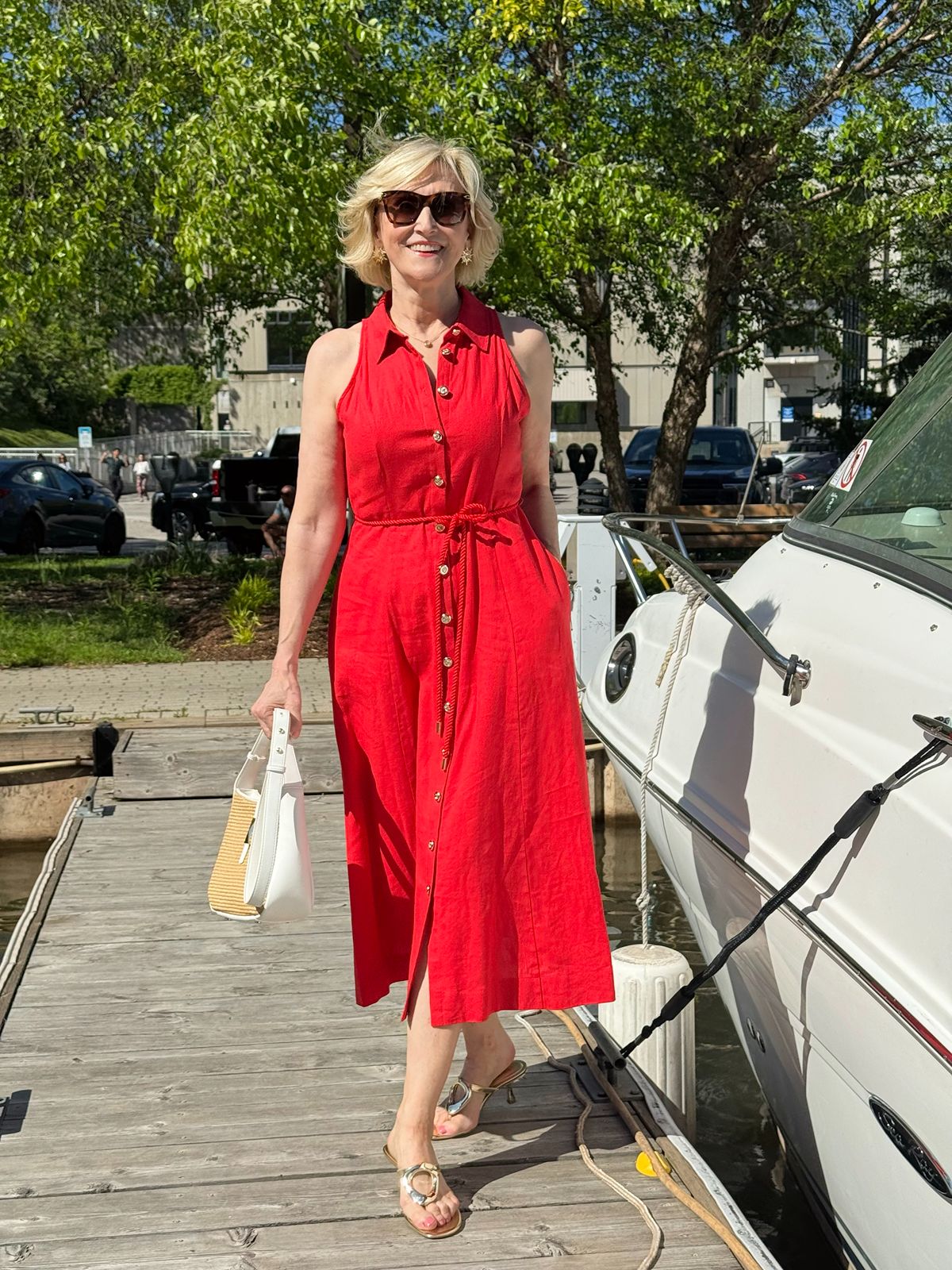 Deborah Boland wearing a red linen shirtdress with a woven handbag and metallic sandals for a chic coastal style outfit.