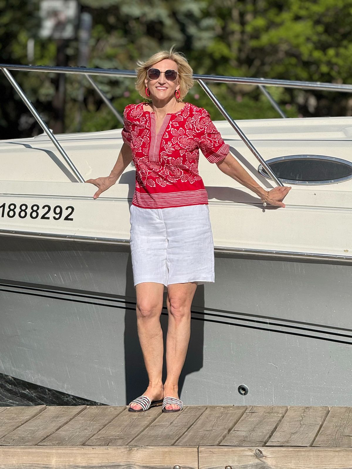 Deborah Boland wearing a red floral top, white linen shorts, and striped sandals in a classic nautical style outfit for summer.