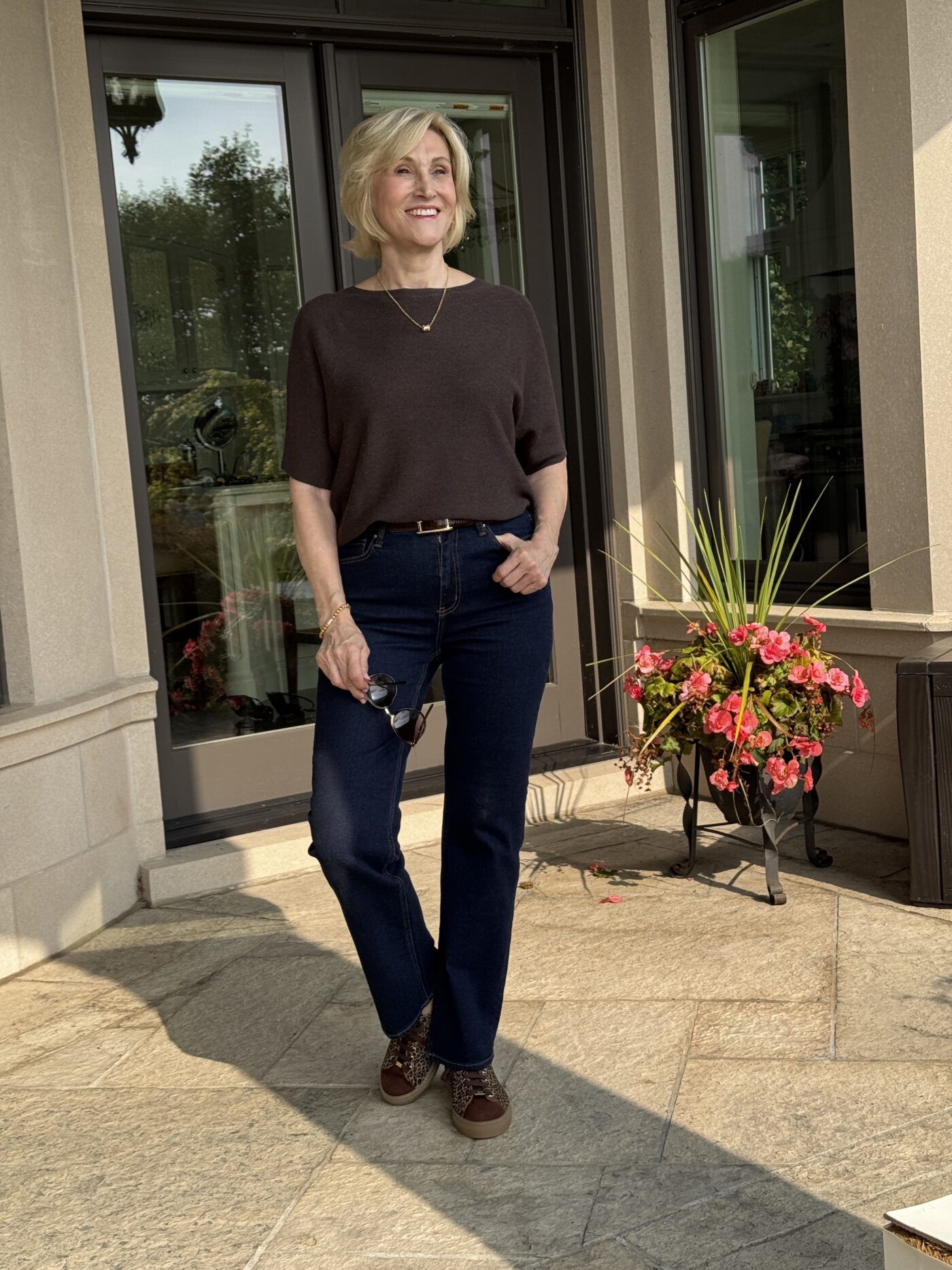 Deborah Boland wearing a chocolate brown sweater with dark wash jeans and leopard print sneakers