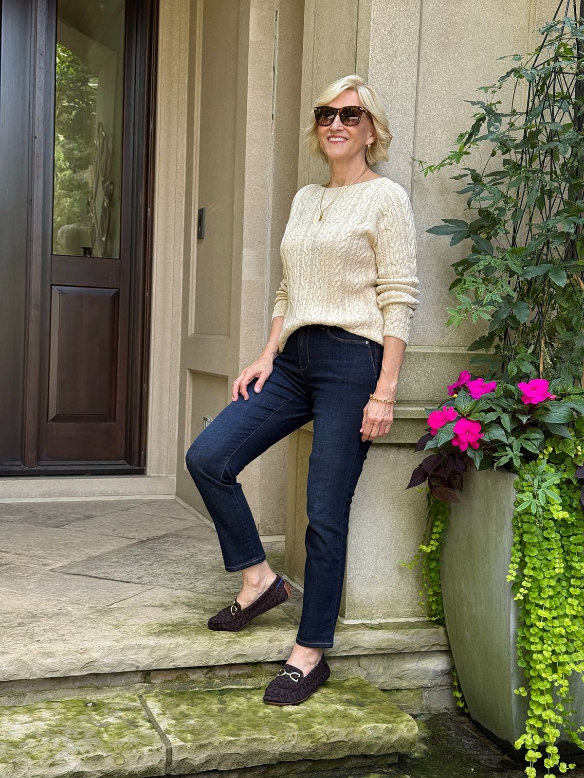 Dark wash slim-leg jeans outfit with a cream cable-knit sweater and loafers for women over 50