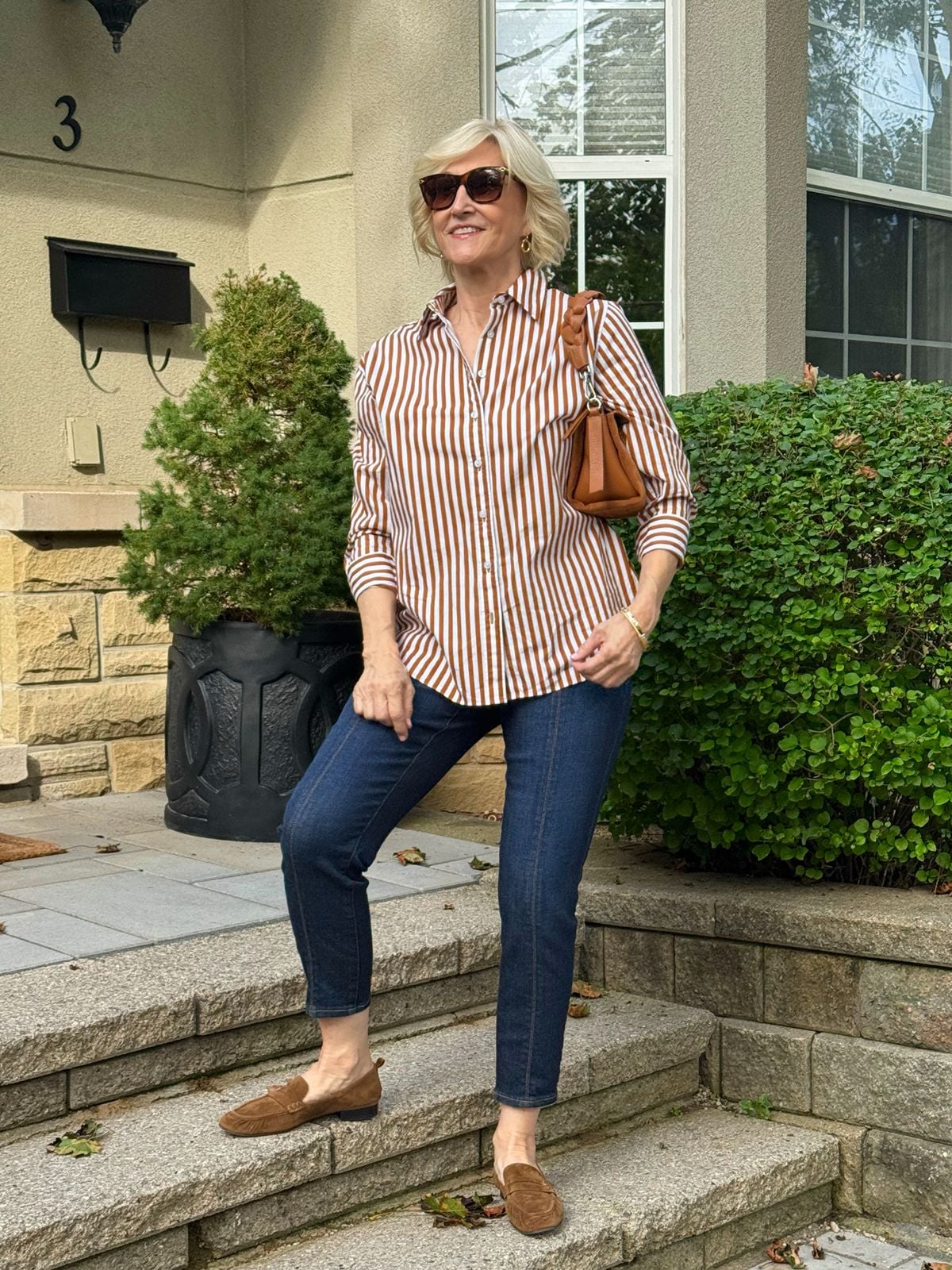 Dark wash ankle jeans styled with a brown striped button-down shirt and suede loafers for fall