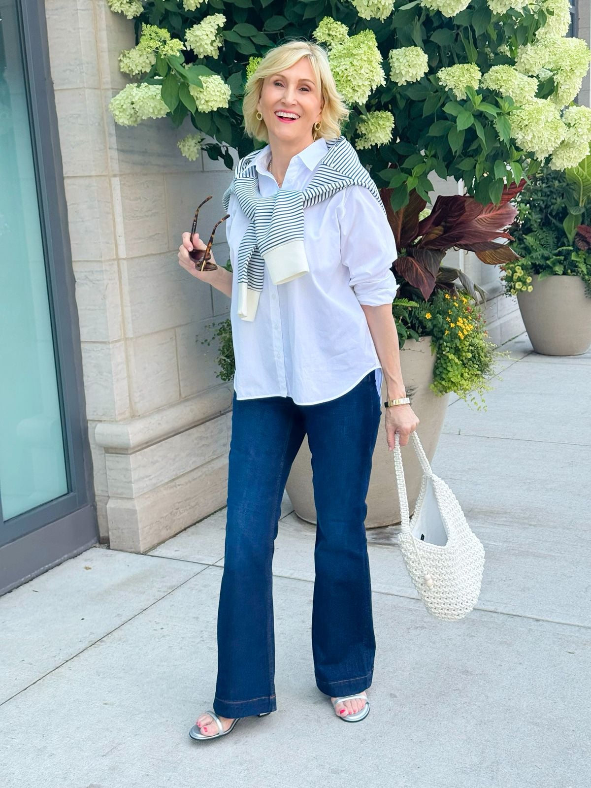 Dark wash flare jeans outfit for women over 50 with a white button-down shirt and striped sweater